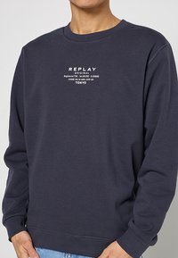 Marineblauw sweatshirt gemaakt van katoenmix, met lange mouwen, geribbelde manchetten en een witte bedrukte logo op de borst.