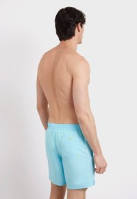 Pantaloni da bagno azzurri con cintura elastica, tasche laterali e tasca posteriore. Il tessuto è liscio e ha un colore uniforme senza motivi.