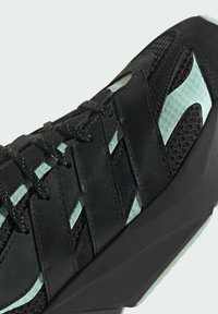 Sort atletiksko med teksturerede overflader, mintgrønne detaljer, tyk snøringssystem og et geometrisk gummisål design.