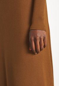 Main noire à la peau foncée avec des ongles courts reposant contre un vêtement en tissu côtelé marron à manches longues.