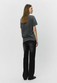 T-shirt in cotone grigio e jeans a gamba larga neri. L'outfit presenta un design semplice con una vestibilità rilassata e senza motivi o abbellimenti visibili.