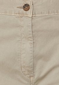 Beżowe bawełniane szorty z zapięciem na guzik z przodu, charakteryzujące się gładką fakturą, przeszyciami oraz zakrzywionymi otworami kieszeni.