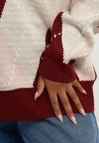 Neulepaita, jossa on vaaleanpunaisia, kerma- ja burgundinvärisiä geometrisia kuvioita; urheilulliset hihansuut ja helma; pehmeä rakenne ja keskipainoinen kangas.