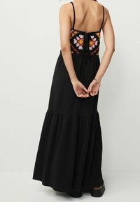 Robe maxi avec une jupe noire fluide et un buste en crochet coloré et à motifs. Elle dispose de bretelles réglables et d'un détail de dos noué.