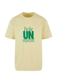 Yellow cotton t-shirt with short sleeves, featuring green text: "Do the UN expected." Classic crew neck design.