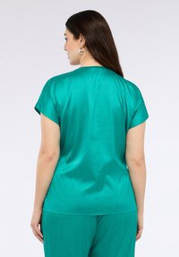 Turkusowa satynowa bluzka z krótkimi rękawami, prosty design i gładka tekstura; posiada szczegół szwu z tyłu oraz luźny krój.