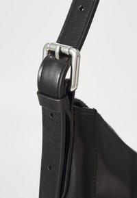 Sangle de sac en cuir noir avec une boucle en métal argenté et des détails de couture, affiche une texture lisse et une longueur ajustable.