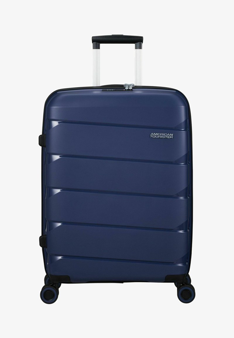 Navy hardshell suitcase with textured surface, diagonal grooves, black accents, retractable handle, and four spinner wheels.