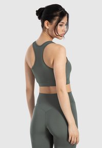 Top deportivo verde oliva con diseño de espalda de nadador y textura suave, combinado con leggings de cintura alta a juego que presentan un sutil detalle de costura.