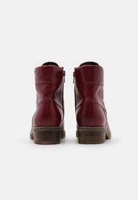 Botas de tobillo de cuero rojo con un acabado suave, cremalleras laterales y tacones de bloque de madera. Costura detallada alrededor de la suela.