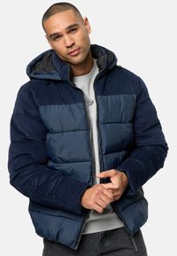 Navy puffer jacket with corduroy accents, featuring a zip closure and hood. Textured fabric, padded sections, and ribbed cuffs.