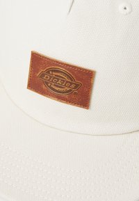 Bijela pamučna baseball kapa s teksturiranim materijalom, s smešnim kožnim zakrpom na kojoj se nalazi logo "Dickies".