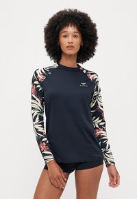 Rash guard à manches longues en bleu marine foncé avec des manches à motif floral, présentant un design ajusté et un logo Roxy sur la poitrine. Texture lisse.