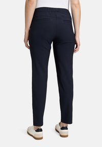 Sötétkék, gumis derekú nadrág, testhez simuló fazonnal, két hátsó zsebbel és szűkített szárakkal. Puha anyag, sima textúrával.