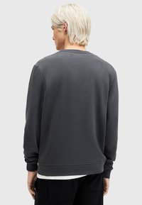 Sudadera gris con un corte relajado, puños y dobladillo acanalados. Tejido suave, diseño de cuello redondo y detalles de costura visibles en la parte posterior.