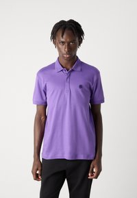 Lila bomullspolo med klassisk krage, korta ärmar och en diskret logotypdetalj på bröstet. Mjuk textur och figurnära design.