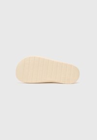 Såle i off-white gummi med et teksturert rutenettmønster for grep. Rund form med logodetalj nær hælen.