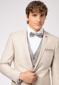 Veste de costume beige avec un gilet gris clair et une chemise blanche. Comprend un nœud papillon gris et un mouchoir de poche. Tissu doux avec une texture lisse.