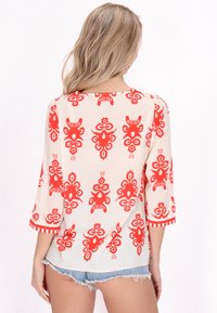 Blusa fluida in crema con un audace motivo floreale rosso, maniche a tre quarti e scollo rotondo con dettagli a strisce sui polsini.