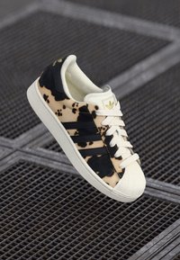 Baskets à motif noir et blanc avec une tige texturée, présentant trois rayures noires, des lacets blancs et un capuchon en caoutchouc.