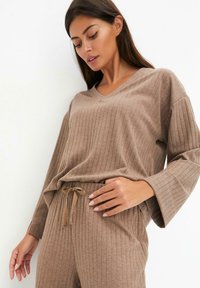 Ensemble de loungewear en tricot côtelé marron comprenant un haut à col en V avec des manches larges et un pantalon assorti avec une taille élastique à cordon réglable.