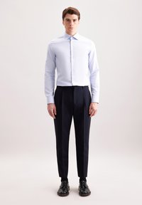 Camicia azzurra chiara a maniche lunghe con chiusura a bottoni, abbinata a pantaloni scuri su misura e scarpe nere, creando un outfit formale.