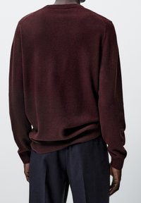 Tummanpunainen neulepaita pyöreällä pääntiellä, pitkillä hihoilla ja resorireunuksilla. Pehmeä koostumus ja rento istuvuus, yhdistetty tummiin housuihin.