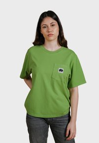 Camiseta de algodón verde con cuello redondo y mangas cortas, que presenta un pequeño logo de elefante en un bolsillo en el pecho. Corte casual.