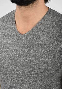 Camiseta gris de pico hecha de una tela suave y texturada. Presenta un patrón jaspeado y un corte relajado en el cuello y los hombros.
