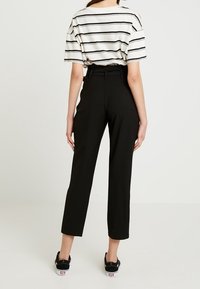 Pruhovaná tričko s krátkým rukávem v krémové a černé barvě; černé kalhoty s vysokým pasem a rovnými nohavicemi; černé tenisky. Jednoduchý design a střih.