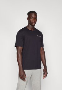 Sort bomulds T-shirt med rund hals og korte ærmer, med et lille rødt og hvidt logo på brystet og ærmet.