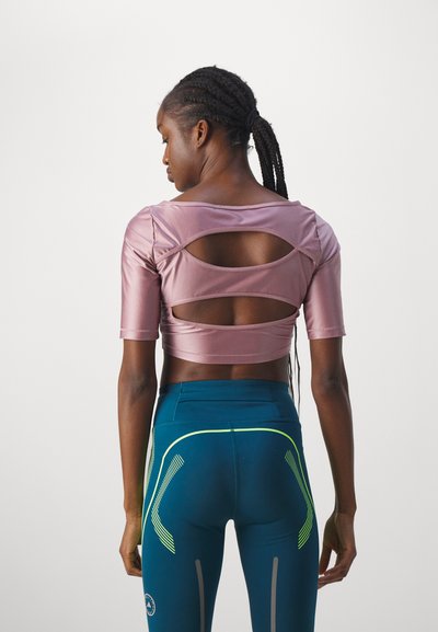 T-skjorte med korte ermer i rosa med utskjært ryggdetalj, kombinert med blå leggings med grønne og grå akcentlinjer. Glatt tekstur.