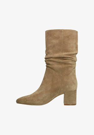 Taupe suède enkellaars met een slouchy ontwerp, puntige neus en blokhak. Vanzelfsprekend textuur met naaddetails aan de zijkanten.