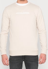 Felpa beige chiaro realizzata in tessuto morbido, con scollo rotondo, polsini e vita a costine, e un logo bianco del brand sulla parte anteriore.