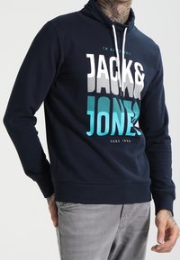 Felpa con cappuccio blu navy con una grande stampa grafica bianca, grigia e turchese. Realizzata in materiale morbido con orlo a costine.