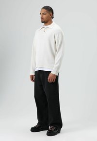 Cream, textured long-sleeve polo with a collar and two buttons, layered over a white shirt. Paired with loose black jeans and black boots.