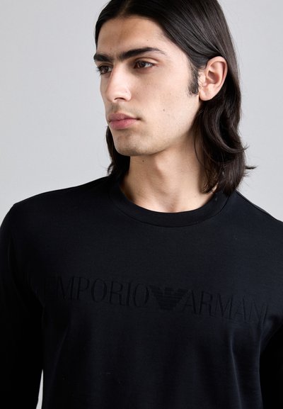 T-shirt preto de mangas longas, feito de um tecido suave, com um logótipo em relevo "EMPORIO ARMANI" na zona do peito e um clássico decote redondo.