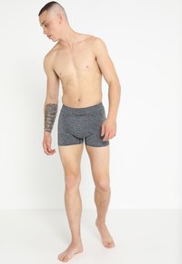Grijze boxers gemaakt van een zachte, rekbare stof, met een gladde tailleband en een aansluitend ontwerp, gedragen door een staande man met een tatoeage.