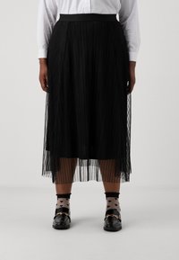 Plisserad svart kjol i lätt material som når till mitt på vaden, bärs över svarta strumpor med hjärt-mönster och svarta loafers med guldaccenter.