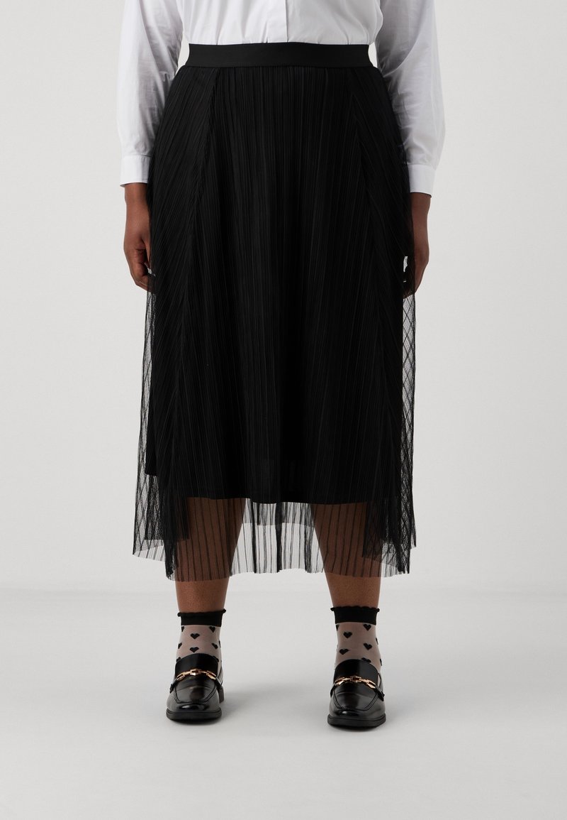 Plisserad svart kjol i lätt material som når till mitt på vaden, bärs över svarta strumpor med hjärt-mönster och svarta loafers med guldaccenter.