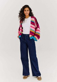 Wielokolorowy sweter z dzianiny w paski w kolorach różowym, niebieskim i żółtym, noszony na białej koszuli i zestawiony z ciemnoniebieskimi spodniami typu wide-leg.