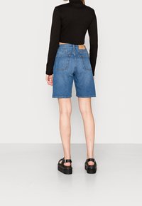 Džínové šortky v světle modré barvě, s rovný střih, pěti kapsami a hnědou koženou etiketou na zadní straně. Kombinováno s černým topem s dlouhým rukávem.