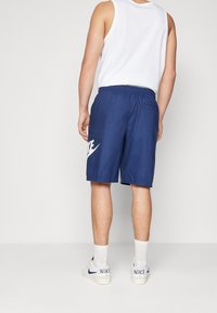 Granatowe szorty Nike z elastycznym pasem, białym logo Nike na lewej nodze oraz gładką, lekką fakturą tkaniny.