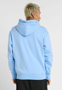 Lyseblå hættebluse lavet af blødt stof, med en stor hætte og ribbede manchetter. Designet er enkelt uden synlige mønstre eller detaljer.