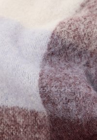 Pehme materjal, millel on tekstureeritud pind, kreemi, lavendli ja sooja pruuni värvi toonides, näidates kogu pinnal peent ruudulist mustrit.