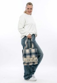 Blaue und beige karierte Handtasche mit Fransen, aus weichem Stoff gefertigt. Zwei robuste Tragegriffe für einen einfachen Transport. Lässiger Stil, kombiniert mit einem Jeans-Outfit.