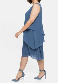 Robe bleue à couches en tissu léger avec une coupe fluide, dotée d'un ourlet incurvé. Associée à des chaussures à talons hauts bleues assorties.