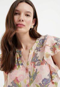 Blumenbluse aus leichtem Stoff mit einem pinken Hintergrund, verziert mit bunten Blumen, Volantärmeln und einem Knopfverschlusskragen.
