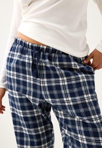 Navyblå och vita rutiga pyjamasbyxor med elastisk midja, justerbar dragsko och sidfickor, tillverkade av mjukt flanelltyg.