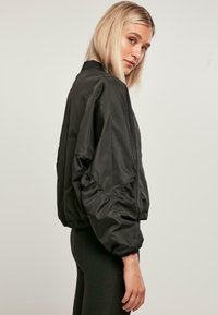 Black bomber jacket with a lightweight, shiny finish. Features a relaxed fit, puffed sleeves, and elastic cuffs and hem. No closures visible.